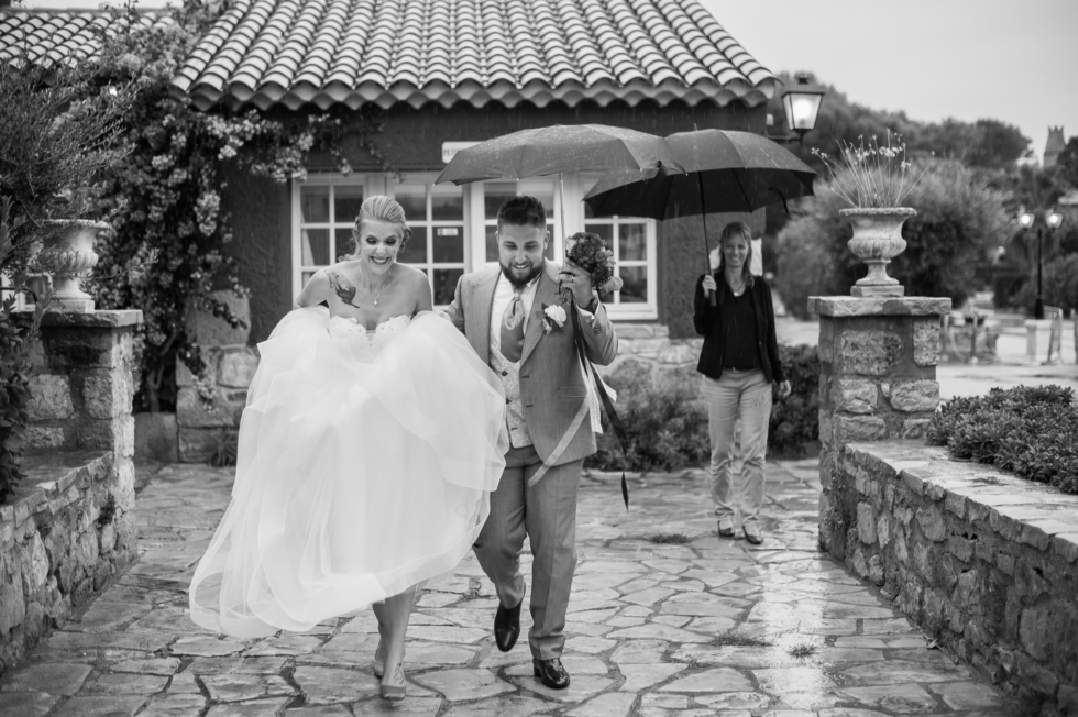 Anecdote un couple de mariés marchand sous la pluie avec un parapluie. elle lève sa robe pour ne pas la mouiller