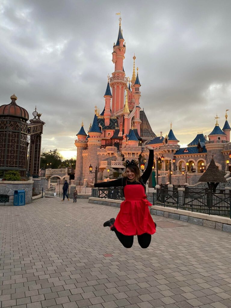 2022 une jeune fille en robe rouge sautant devant le château de Disney
