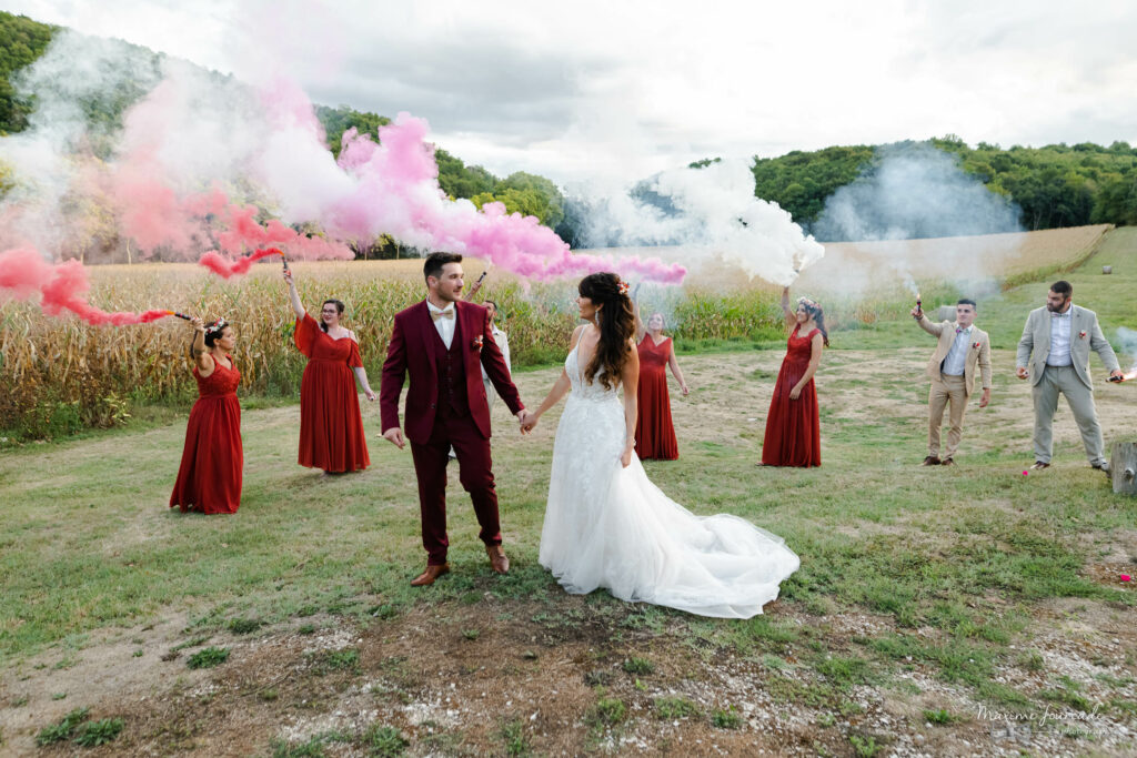 Cortège mariage photo de couple des mariés avec lur cortège en fond qui allument des fumigènes