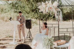 Le marié prononçant ses voeux au pupitre avec la mariée assise qui l'écoute.